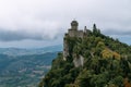 View from the top of the mountain to the medieval fortification. Dramatic mystical weather with fog. Castle in San Marino Seconda