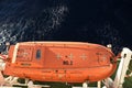 View from top on the orange colour life boat with reflective tape stickers secured with davits and safety hooks. Royalty Free Stock Photo