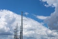 View of the tops of several metal electrical poles, each carrying multiple lines, against a blue sky with white clouds