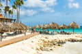 View of tourists on sun beds under sun umbrellas on white sandy beach near hotel.