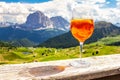 View of the traditional Italian alcoholic drink Aperol Spritz on the background of colorful Italian meadows and the Dolomites Alps