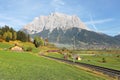 View of a train traveling through green fields with rugged Zugspitze Mountain in background on a beautiful sunny day in Lermoos