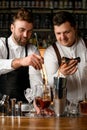 view on mixing cup with cold cocktail that bartender stirs and another bartender pours drink into jigger Royalty Free Stock Photo