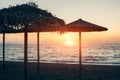 View of tropical beach with big straw umbrellas and sun loungers on the sunset sea background Royalty Free Stock Photo