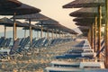 View of tropical beach with big straw umbrellas and sun loungers on the sunset sea background Royalty Free Stock Photo