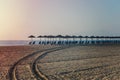 View of tropical beach with big straw umbrellas and sun loungers on the sunset sea background Royalty Free Stock Photo