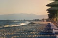 View of tropical beach with big straw umbrellas and sun loungers on the sunset sea background Royalty Free Stock Photo