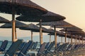 View of tropical beach with big straw umbrellas and sun loungers on the sunset sea background Royalty Free Stock Photo