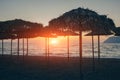 View of tropical beach with big straw umbrellas and sun loungers on the sunset sea background Royalty Free Stock Photo