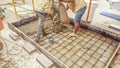 View of two construction workers spreading concrete on the floor on top of iron mesh armor