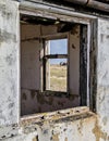 View through two delapidated windows in a hut on a beach looking towards a derelict boat