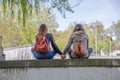 View of two girlfriends girls sitting on a wall and looking at the landscape hand in hand and lovingly