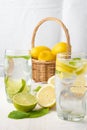 View of two glasses of water with lemon and lime slices with ice cubes on white wood, half lemons, mint and basket in the backgrou Royalty Free Stock Photo