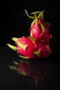View of two pink pitayas or dragon fruits on black table with reflection and black background,