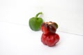 View of two shiny, wet, red bell peppers next to a faded green bell pepper on a white background with their lighting and shadows