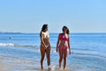 Two young women wearing face masks and bikinis talking to each other while walking close to the sea. Safety and new travel concept Royalty Free Stock Photo