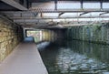 view under an old low steel girder bridge crossing the leeds to liverpool canal near armley with stone wall and a narrow footpath