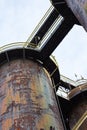 View from underneath walkways spanning between huge stacks of an old steel mill, heavily rusted metal patina