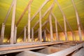 A view on unfinished attic from inside the house with a close-up on wooden ceiling joists, roof beams, rafters, wall studs and