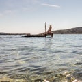 View of unrecognizable woman wearing big summer sun hat tanning topless and relaxing on old wooden pier in remote calm