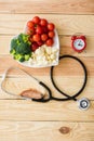 View of vegetables on heart-shape plate near stethoscope and retro alarm clock on wooden surface Royalty Free Stock Photo