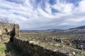 View of the village and mountains from the Medieval fortress on a rock. Stone wall and part of tower. Bright blue sky with clouds Royalty Free Stock Photo