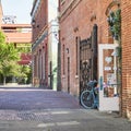 View of a walking street with brick buildings, a black gate, an open white door and a blue bicycle. Royalty Free Stock Photo