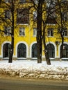 View Of The Wall Of Yellow House With Arched Beautiful Windows Through The Trees And With A Dirty Road In Snow In Winter