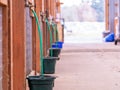 View at water buckets and green hoses hanging down from a faucets near stalls in a walkway