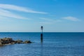 A view of a weathercock in the end of a stony groyne breakwater with a cormorant spreading his wing, crystal blue water and some
