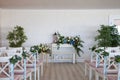 View of a wedding ceremony scene in a room with several rows of white chairs and compositions from different flowers Royalty Free Stock Photo