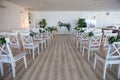 View of a wedding ceremony scene in a room with several rows of white chairs and compositions from different flowers Royalty Free Stock Photo