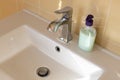 View of a white bathroom sink with a contemporary mixer tap, an unlabeled bottle of liquid soap. Concept of modern interior, water