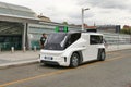 View of a white ETIOCA full electric minivan taxi parked before a modern building