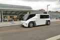 View of a white ETIOCA full electric minivan taxi parked before a station building