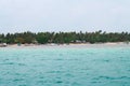 View of white sand beach from a distance with lined up greens & trees in the background