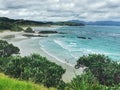 A view on an white sand ocean beach surraunded by green trees under cloudy sky Royalty Free Stock Photo