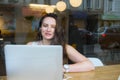 View through the window with city reflection of smiling businesswoman in headset working on laptop sitting in cafe Royalty Free Stock Photo