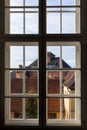 View through window shows historic rooftops with warm tiles and brick structures under soft daylight. Framed composition Royalty Free Stock Photo