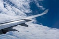 View from a window of the sunlit aircraft wing set against a bright blue sky with dense white clouds. The sharp contrast Royalty Free Stock Photo