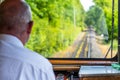 A view from the window of a traveling railroad train, a visible engine driver running a train, dashboard, tracks, trees and a blue