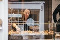 View through the window of a woman putting macaroons in a box inside an artisan bakery in Covent Garden, London, UK.