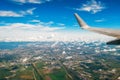 View of the wing of the plane in the porthole on the city and the airport with picturesque clouds.