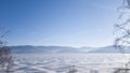 View of the winter lake Baikal: the surface of the lake in the ice, on the other side of the mountain, in the foreground trees.