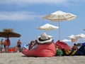 View at Woman from Back Lying on Red Pillow Cushion and Relaxing on Ocean Sand Beach Wearing Straw Hat During Summer Vacation Royalty Free Stock Photo