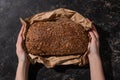 View of woman holding fresh baked loaf of whole grain bread in paper on stone black surface Royalty Free Stock Photo