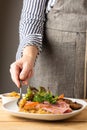 View of woman`s hand with apron putting caramelized onions in a plate of pastrami with salad, on wooden table, Royalty Free Stock Photo