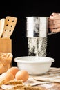 View of woman`s hand with flour falling from a sieve into a bowl, on a rustic table with cloth, eggs, ears of wheat and wooden sp Royalty Free Stock Photo