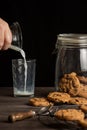 View of woman`s hand pouring milk into a glass, on a wooden table with chocolate cookies, black background Royalty Free Stock Photo