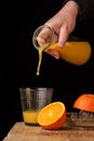 View of woman`s hand serving frozen orange juice with a bottle, over a glass, on wooden table with oranges, black background Royalty Free Stock Photo